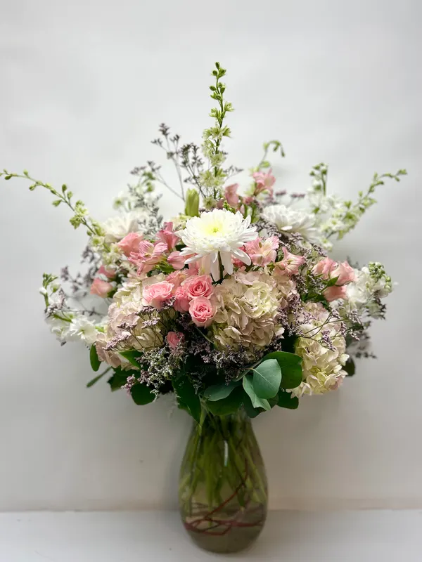 Tall lush pastel arrangement — pink spray roses, blush hydrangea, larkspur and lavender limonium in a glass vase