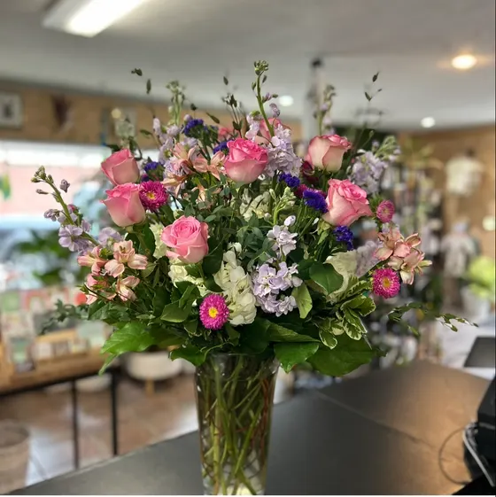Large pink and lavender arrangement on the shop counter, with gift shelves and plants in soft focus behind
